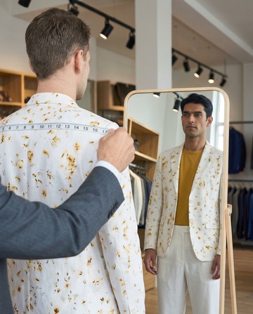 Tailor measuring shoulder width on an eco-printed floral blazer during a made-to-measure fitting session
