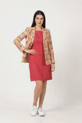 A woman modeling a two-piece outfit consisting of a solid magenta pink knee-length dress and a beige patterned linen blazer with red and gold details, paired with white sneakers, against a plain white studio background.