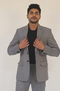 Stylish man in a gray and white checkered cotton jacket and pants, with a black shirt and white sneakers.