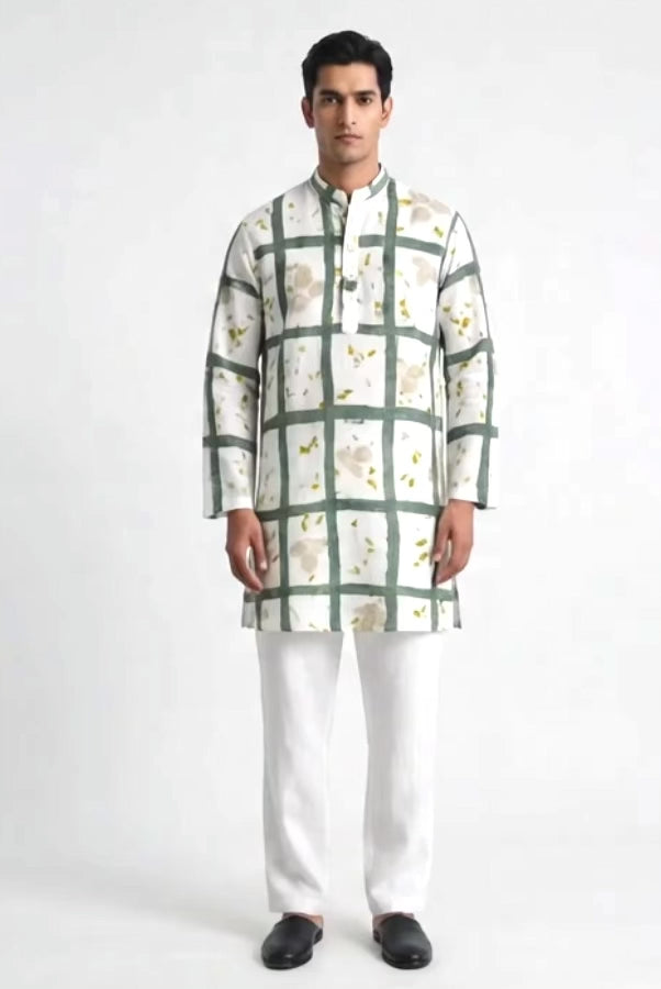 A man modeling a white long-sleeve kurta with a green grid pattern and small yellow floral eco-print accents, paired with white trousers and black shoes, against a light gray studio background.