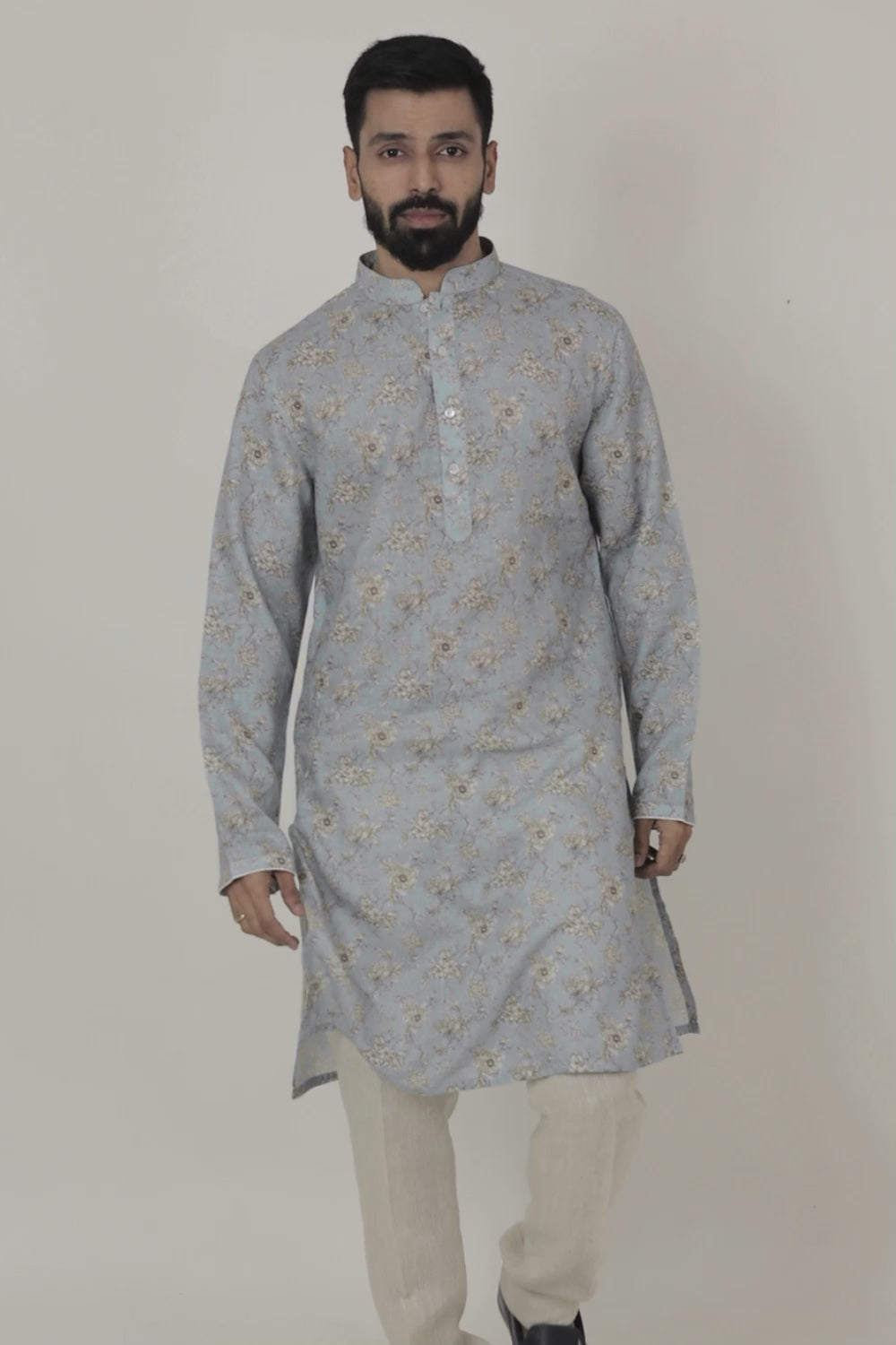 A man wearing a traditional Indian linen kurta with a mandarin collar, featuring a floral print and matching buttons, paired with light-colored trousers.