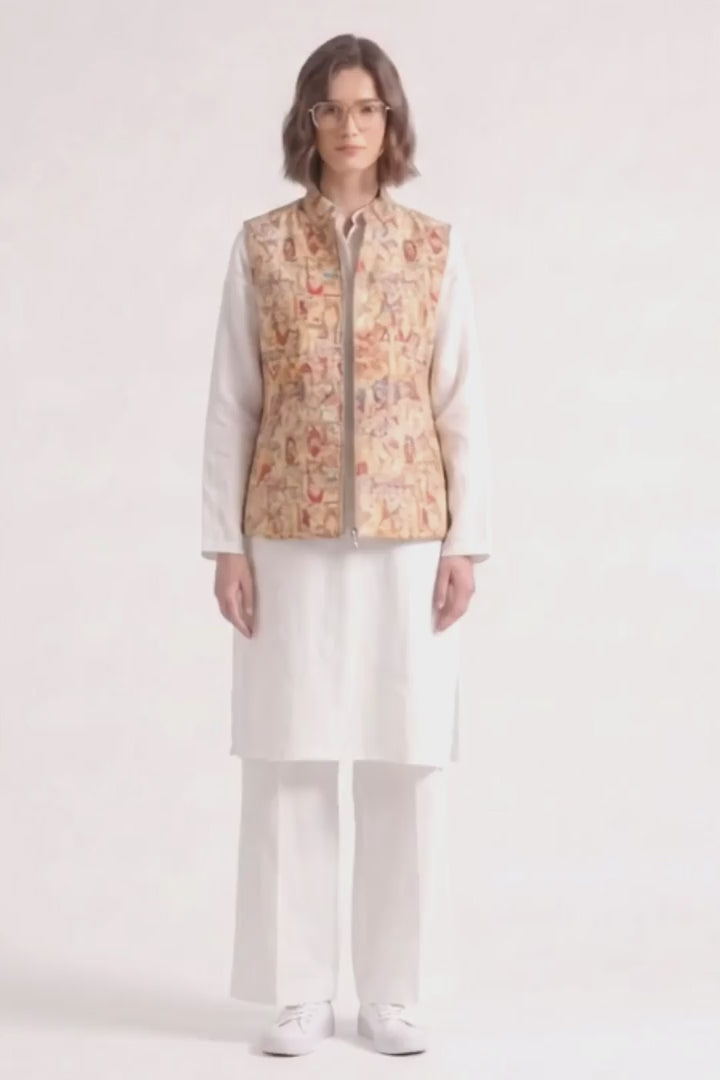 A model wearing a white traditional outfit consisting of a long-sleeve kurta, wide-leg trousers, and white sneakers, layered with a sleeveless  linen  vest featuring a detailed multicolor illustration pattern.