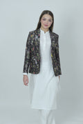 A woman modeling a silk blazer with a floral pattern, wearing a white shirt and pants.