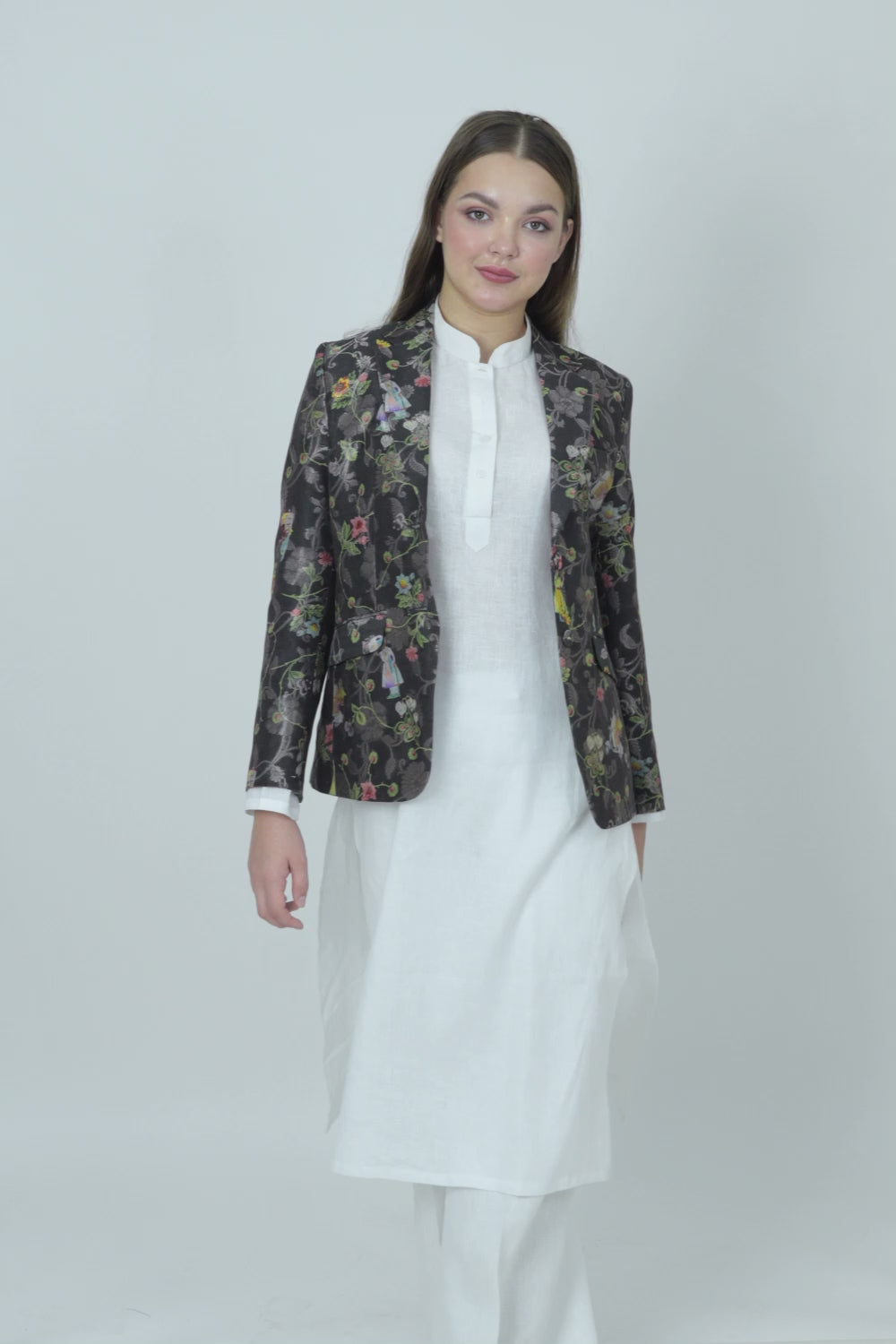 A woman modeling a silk blazer with a floral pattern, wearing a white shirt and pants.