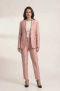 A woman modeling a dusty pink tailored suit set consisting of a silk blazer and matching trousers, styled with a white top and black heels against a light gray studio background.