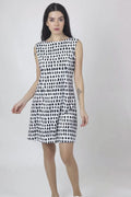 A woman wearing a sleeveless, knee-length black and white hemp dress with a boat neckline, standing before white background