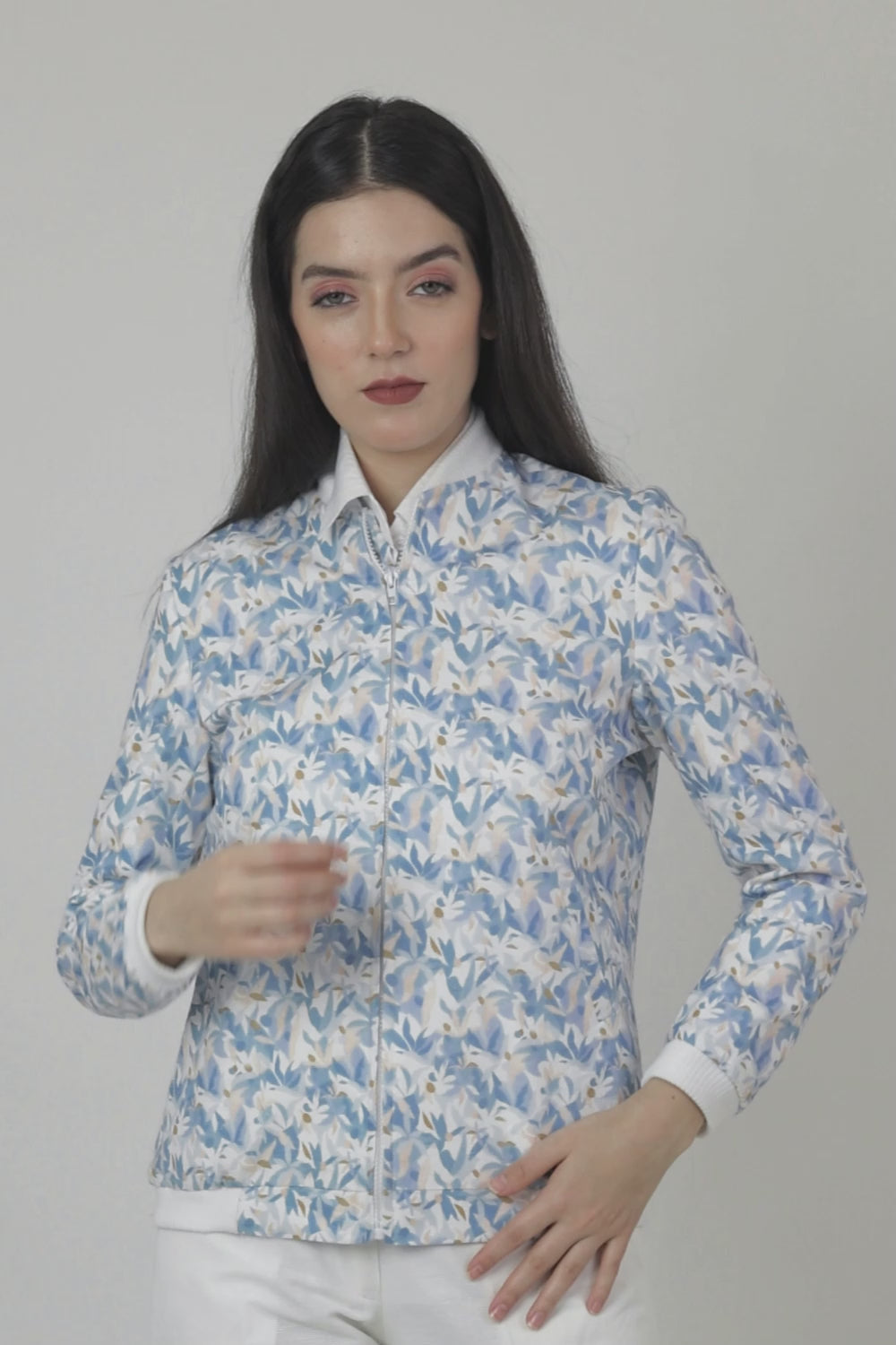 Woman wearing a blue floral Jacket over a white shirt with beige pants on a white background