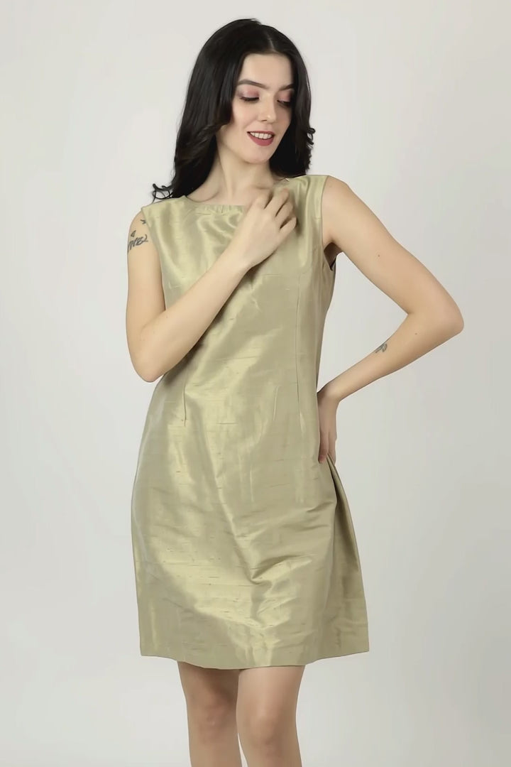 A woman modeling a sleeveless, knee-length A-line silk dress in a metallic gold color, paired with black pointed-toe heels, against a plain white studio background.