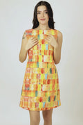 A woman modeling a sleeveless, knee-length hemp dress with a vibrant abstract geometric pattern in orange, yellow, and blue, paired with white sneakers, against a light gray studio background.