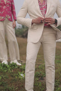 A man wearing white linen trousers with a white jacket and a multicolored shirt, standing against a white background.