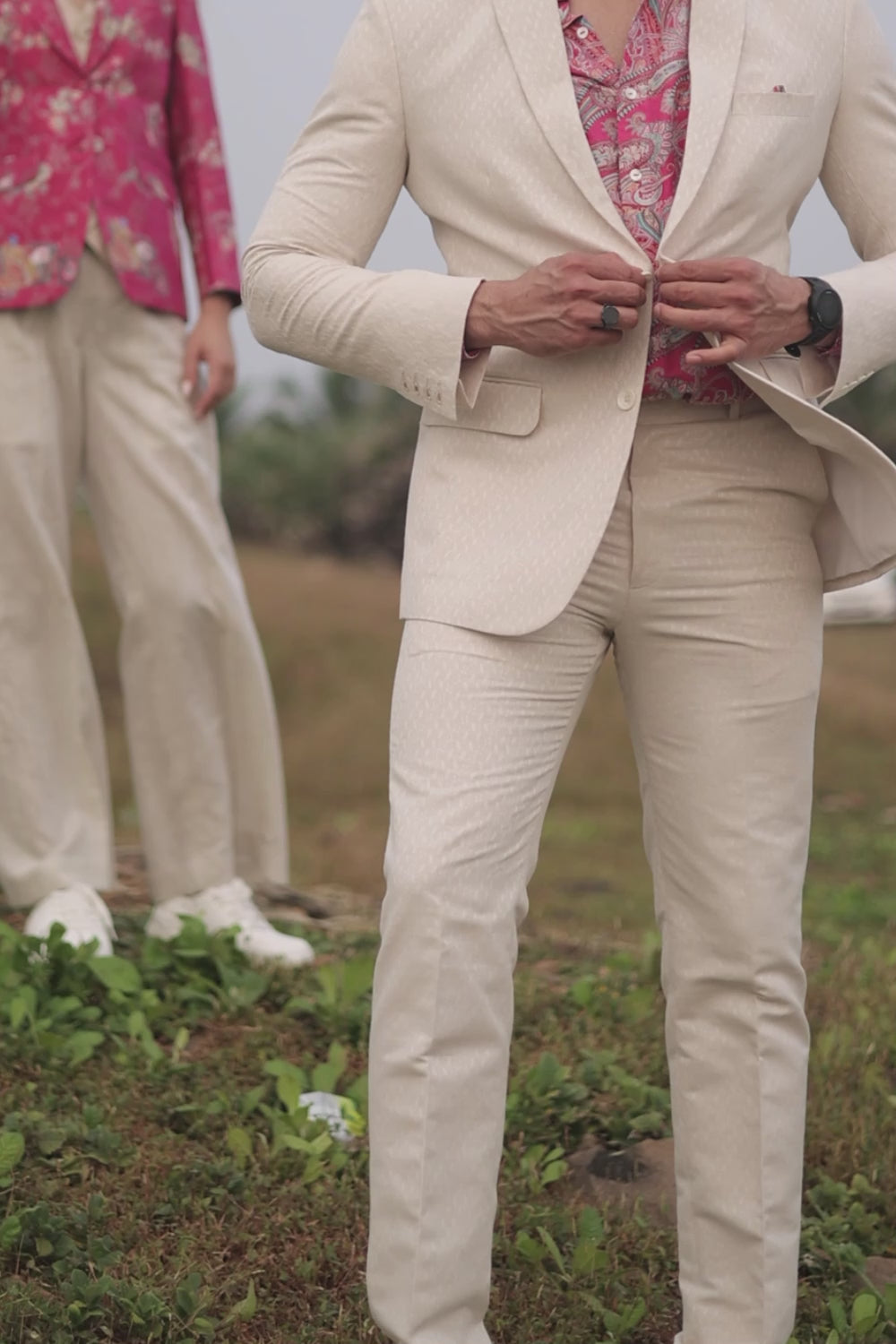 A man wearing white linen trousers with a white jacket and a multicolored shirt, standing against a white background.