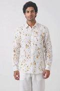 A man wearing a white long-sleeve button-up shirt with a gold abstract floral pattern, posing against a plain white background.