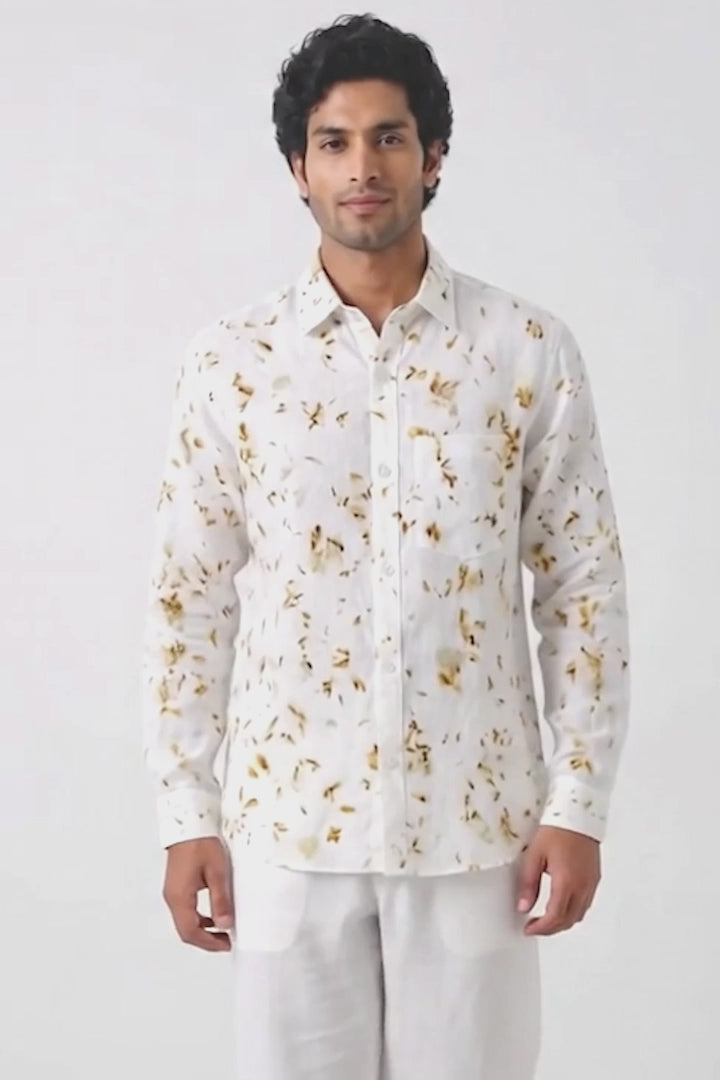 A man wearing a white long-sleeve button-up shirt with a gold abstract floral pattern, posing against a plain white background.