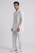 A man modeling a white long-sleeve linen kurta with a split collar and matching white trousers, standing against a plain white studio background.