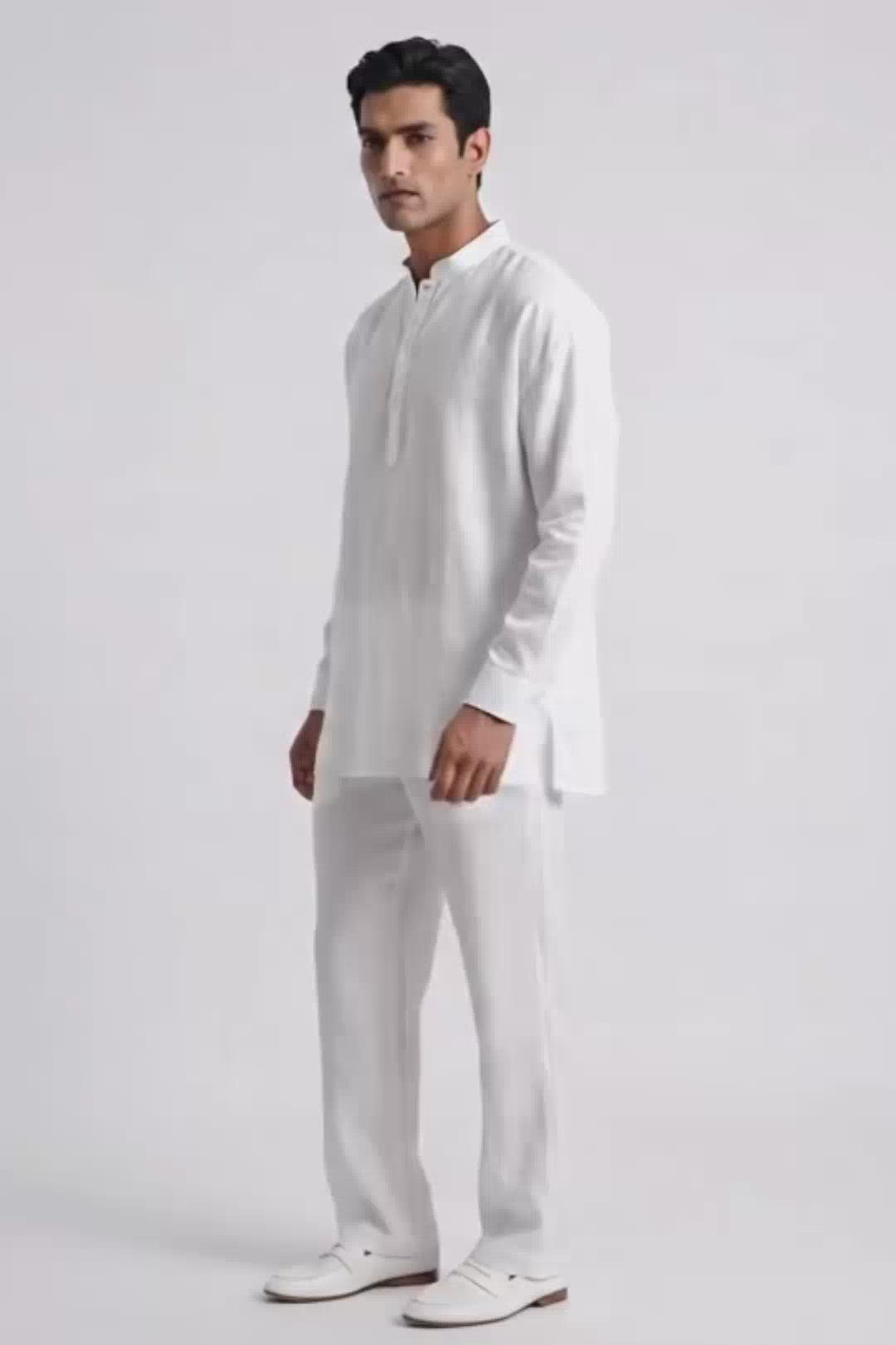 A man modeling a white long-sleeve linen kurta with a split collar and matching white trousers, standing against a plain white studio background.
