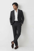 A man wearing a black two-piece hemp suit with a white dress shirt and dark brown loafers, standing against a plain white studio background.