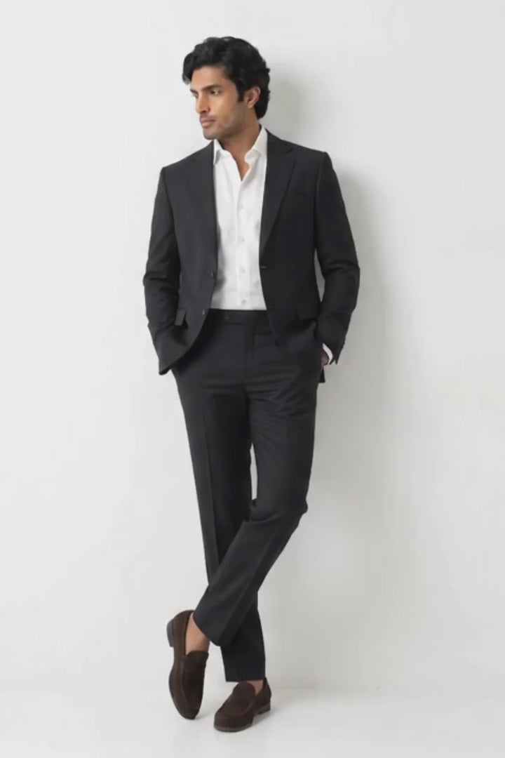 A man wearing a black two-piece hemp suit with a white dress shirt and dark brown loafers, standing against a plain white studio background.