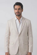 A man modeling a light beige linen suit with a white dress shirt and dark brown loafers, standing against a plain white studio background.