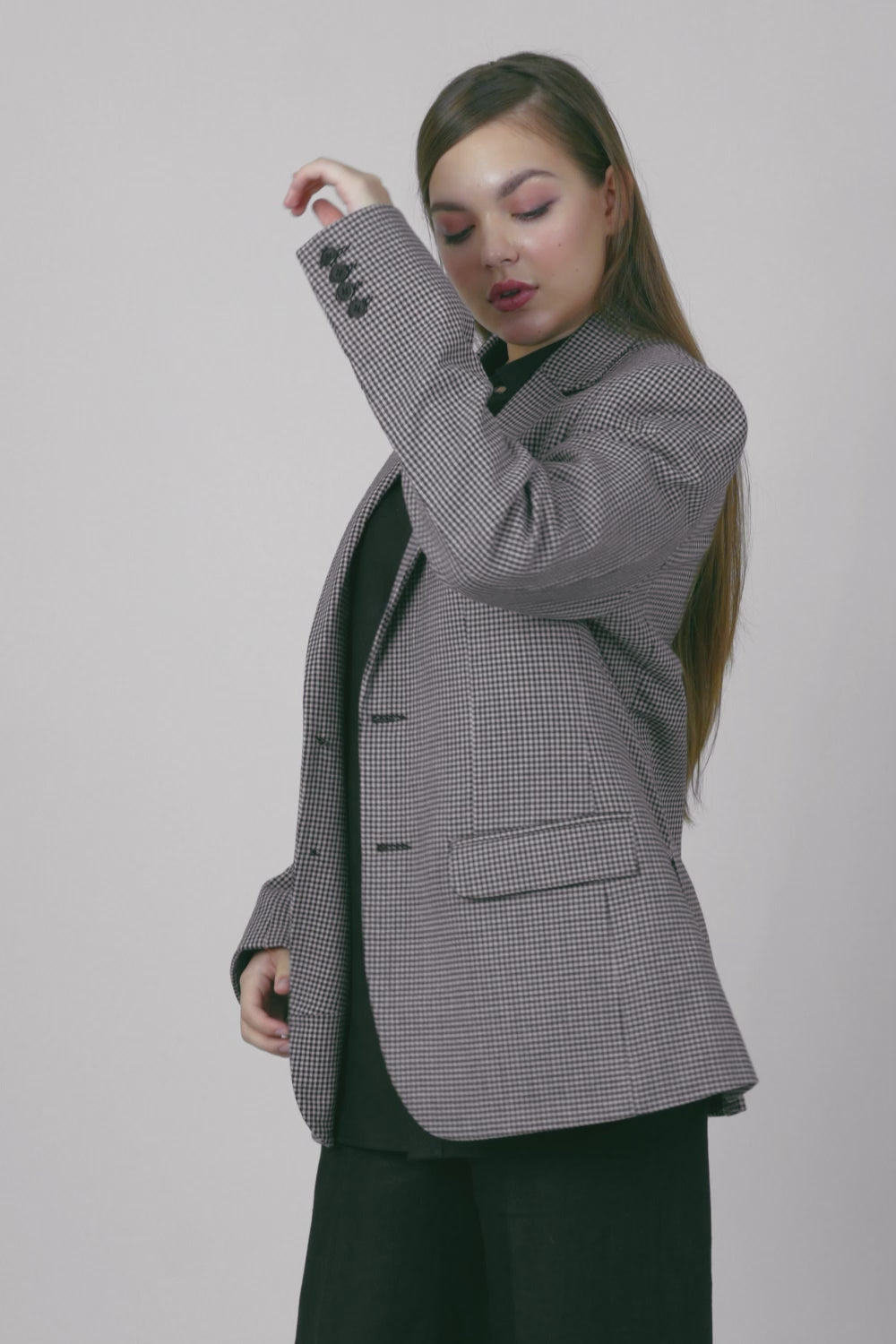 A woman wearing a gray and white patterned cotton blazer, a black button-down shirt, and black wide-leg trousers.