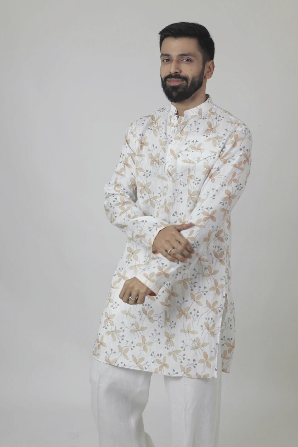 A man wearing a traditional Indian linen kurta with a mandarin collar, featuring a floral print and matching buttons, paired with light-colored trousers.
