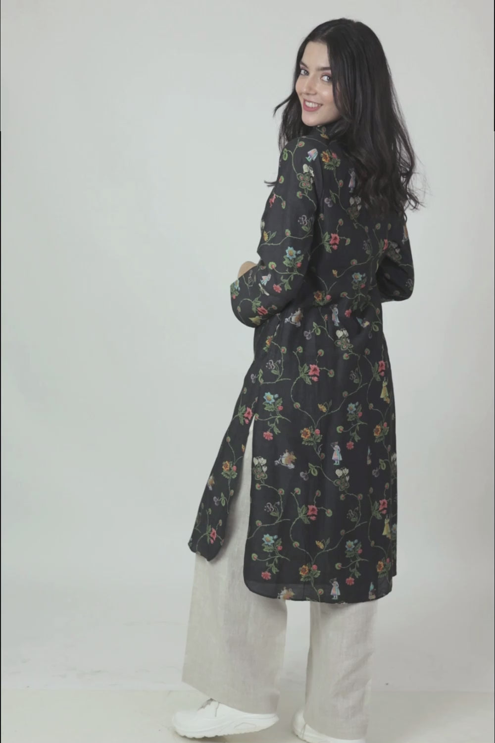 A woman standing against a white background, wearing a floral print long sleeve kurta with a mandarin collar and a V-shaped neck.