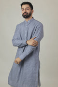 A man wearing a blue linen kurta with a mandarin collar, button placket at the waist, and side pockets. The kurta has a relaxed fit and side slits.