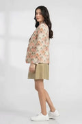 A woman modeling a beige floral linen blazer over a metallic gold midi dress, paired with white sneakers, against a light gray studio background.