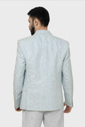 A male model wearing a light blue linen blazer with a Notch Lapel, two buttons, and two patch pockets on the front, paired with light-colored trousers.